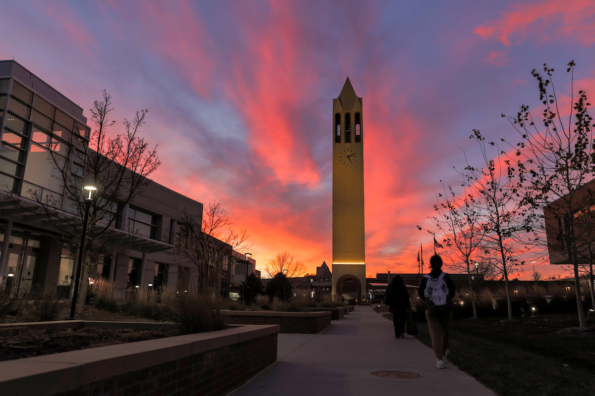 The Henningson Memorial Campanile at sunset as a student walks toward the library.