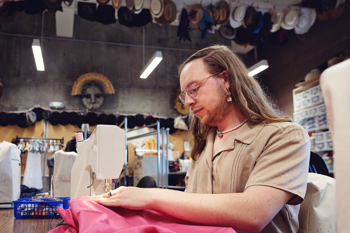 A student sews fabric using a machine in a theatre costume shop.
