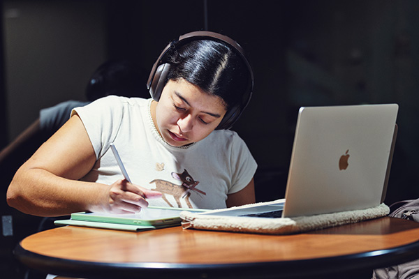 student wearing over the ear headphones is studying on a laptop