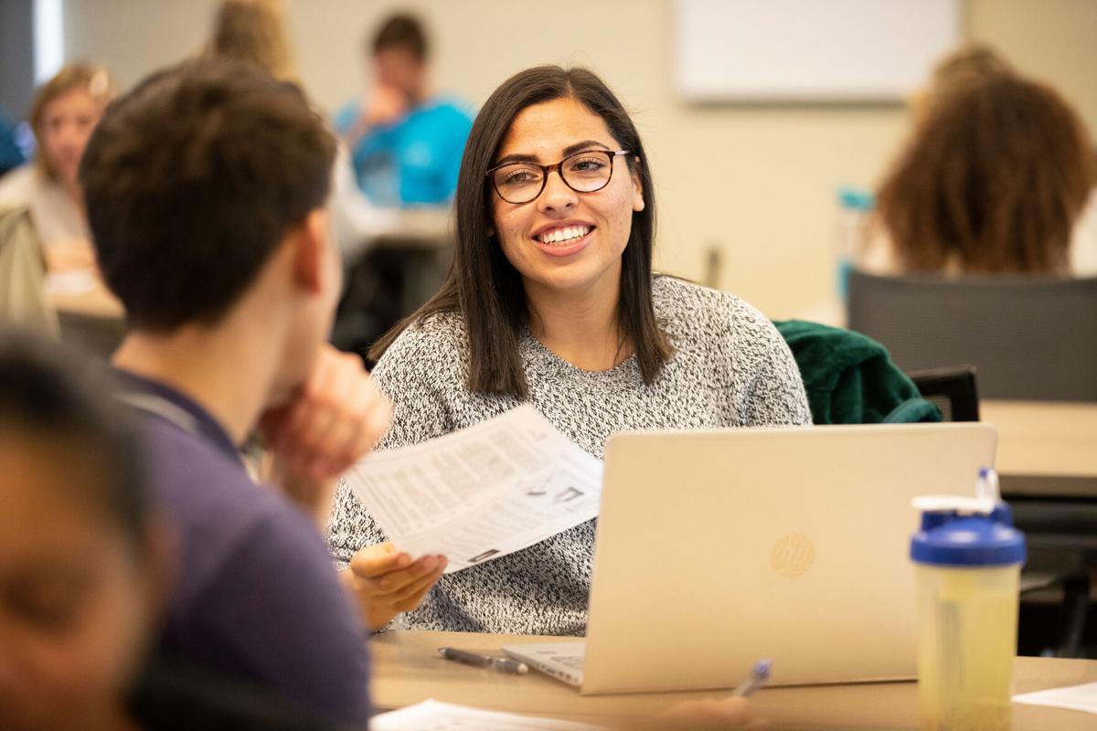 a female student wearing glasses hands a paper to a male student.