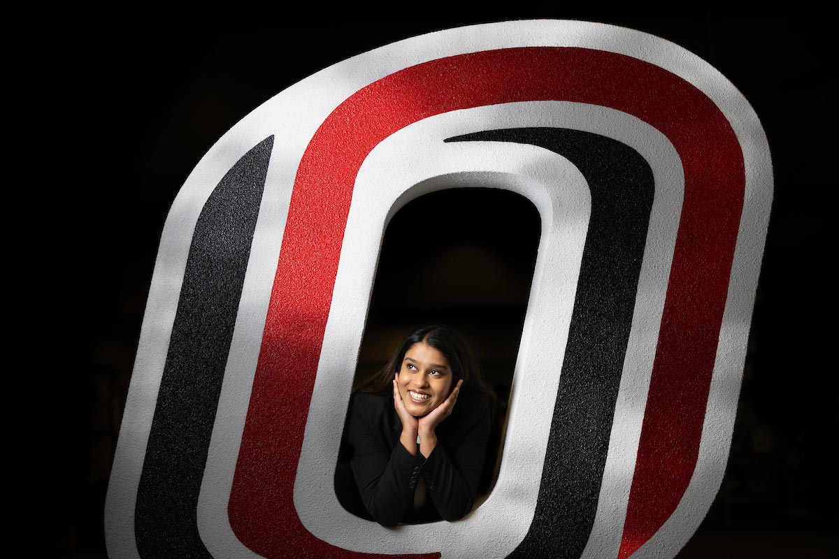 Ishani Adidam, a senior majoring in business administration with a concentration in human resources management, business analytics, and management and leadership, who is the UNO Student Body President and Student Regent, poses with a giant 'O' logo.
