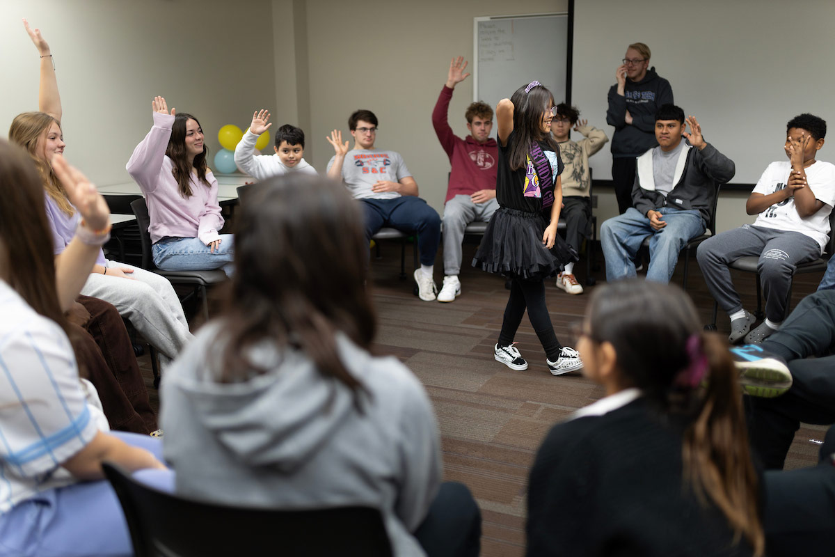 UNO students spend the day working with Kids Can as a part of service-learning. UNO students seated in chairs placed in a circle, with an elementary student in the middle as a part of a game.