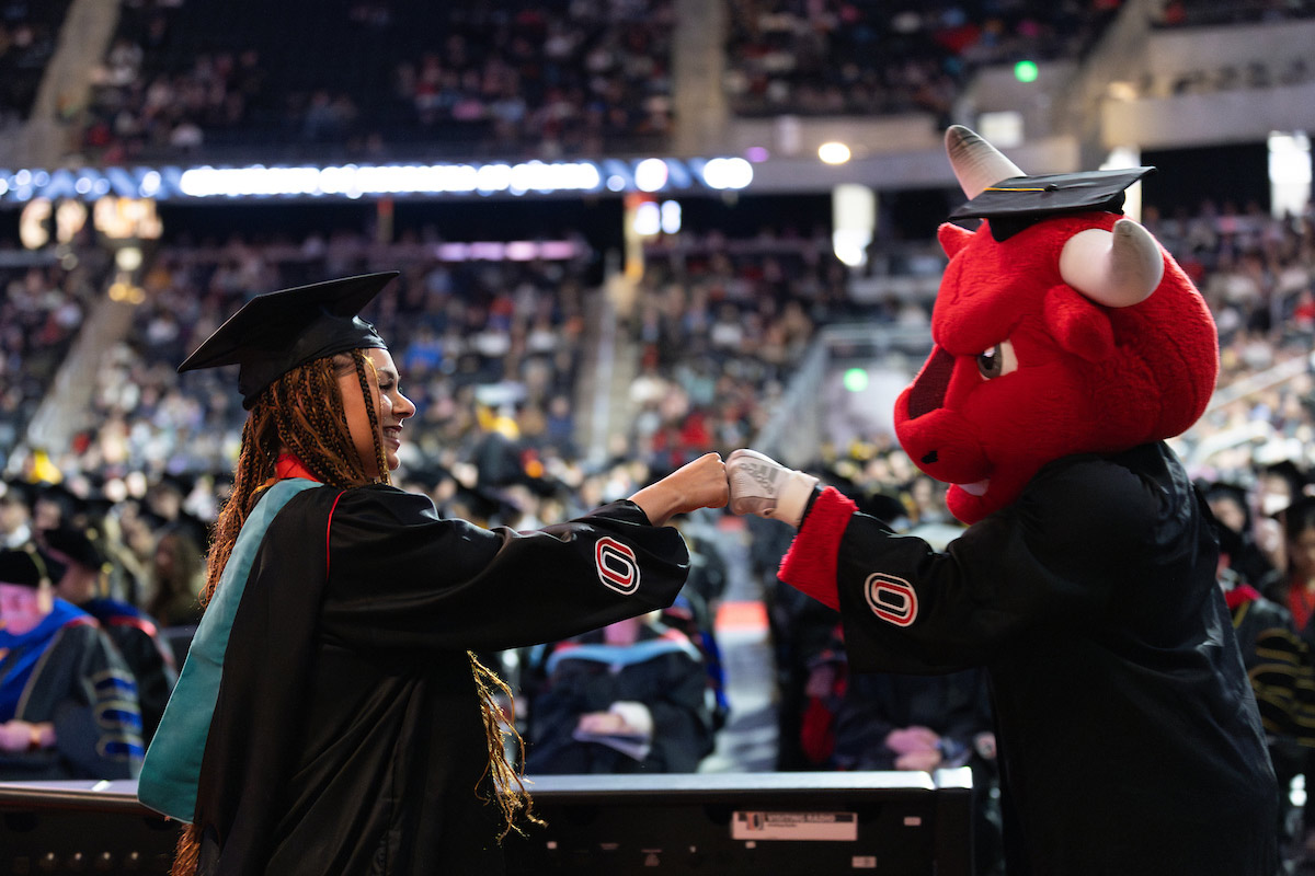 Durango, UNO's mascot, celebrates with a graduate student during UNO’s December 2024 commencement ceremony