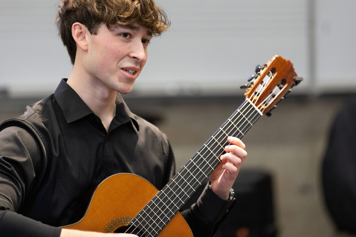 A student dressed in a black shirt plays a classical guitar at the Research and Creative Activity Fair at the University of Nebraska at Omaha on April 11, 2025. He is focused and engaged in his performance.