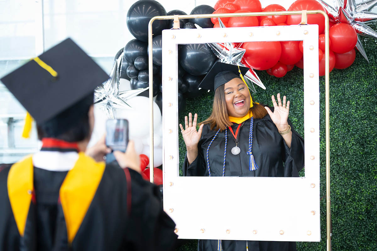 A graduating student poses with a Polaroid frame for a photo before commencement.