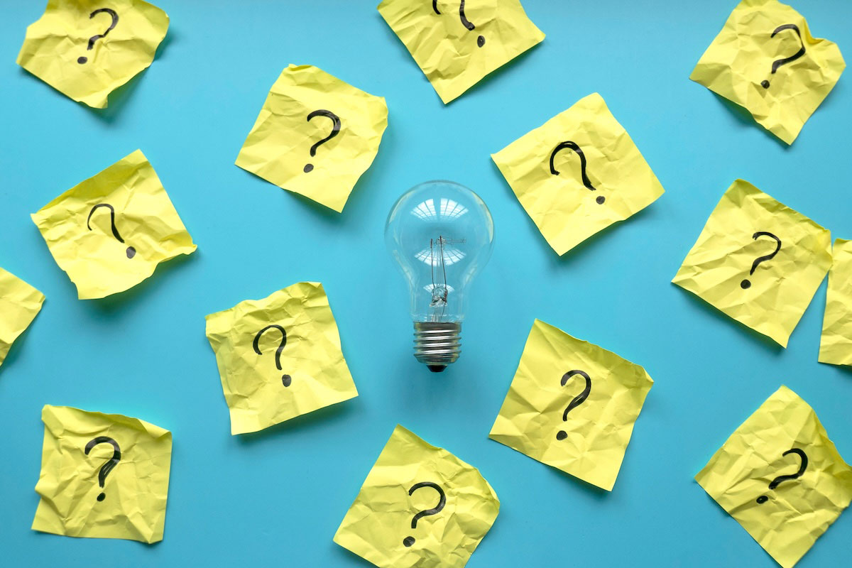 Light bulb surrounded by yellow post-it notes, each with a question mark written on it