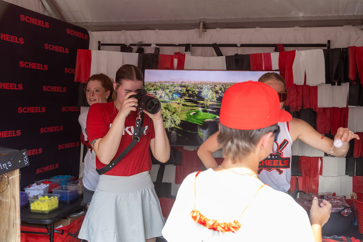 Bella McAtee takes a photo of a young boy at a Scheels booth in the Men's College World Series Baseball Village.