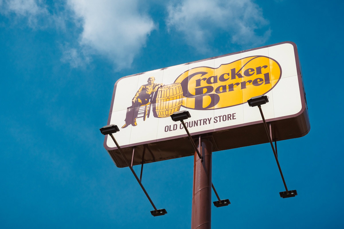 A tall road sign on the highway for a Cracker Barrel restaurant.