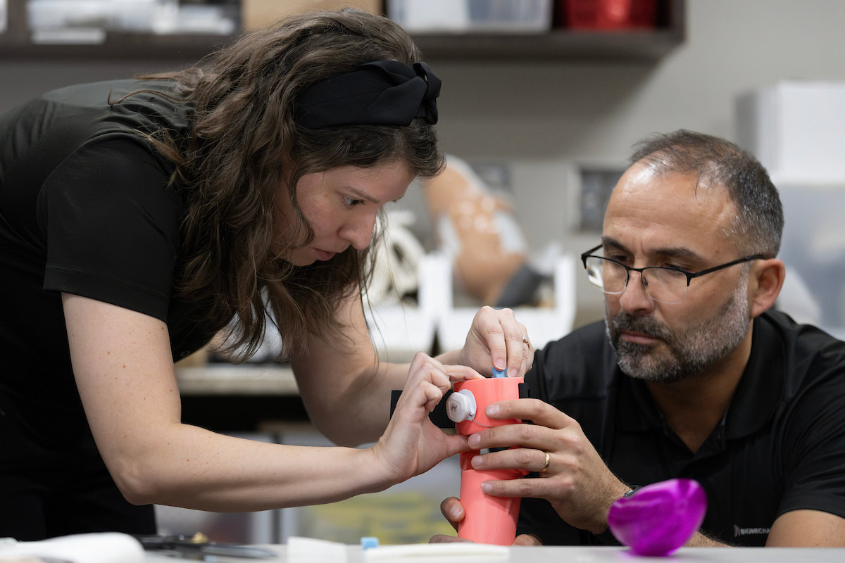Researchers adjust a 3D-printed prosthetic limb with precision tools on a workbench.