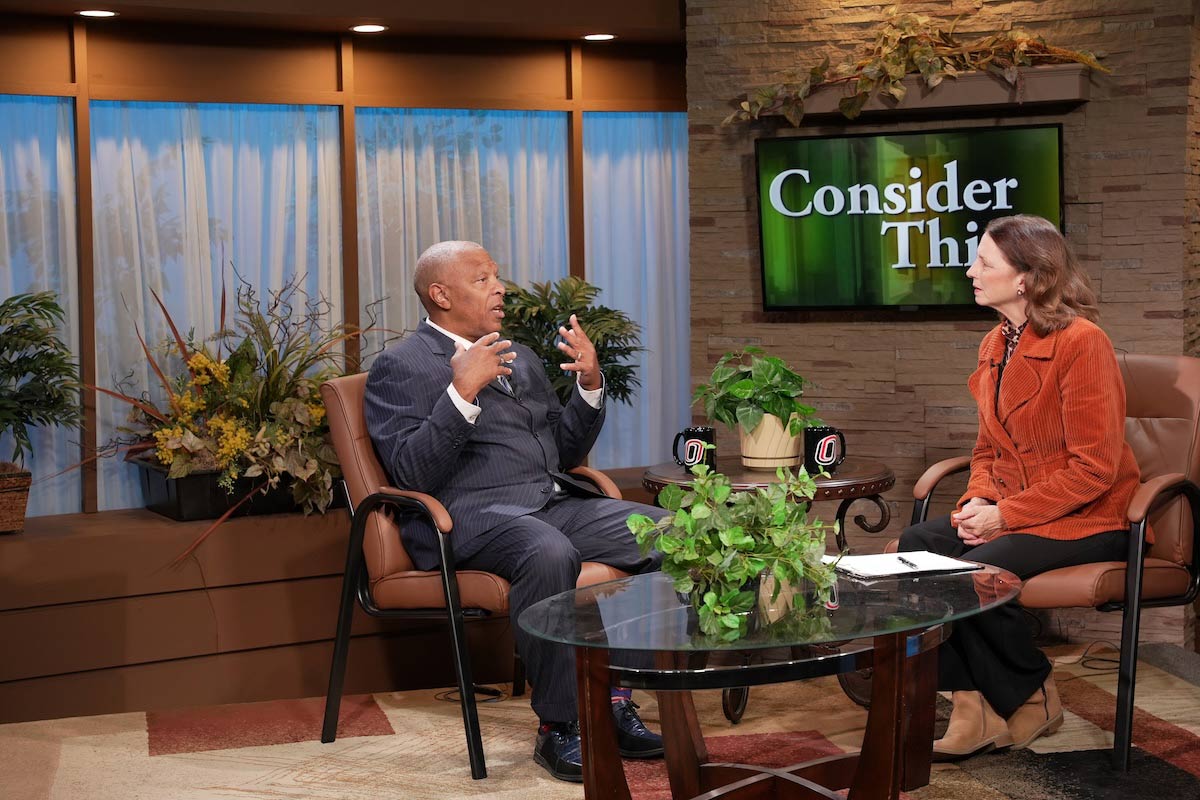 Mayor John W. Ewing, Jr., seated on the left, gestures while speaking with host Cathy Wyatt during a taping of Consider This in the UNO television studio.