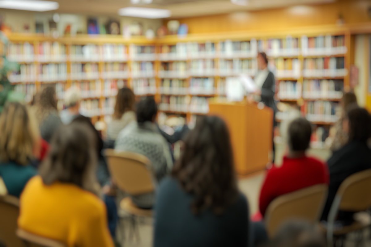 Blurred background of a community library event showcases an engaging reading session with attendees focused on the speaker