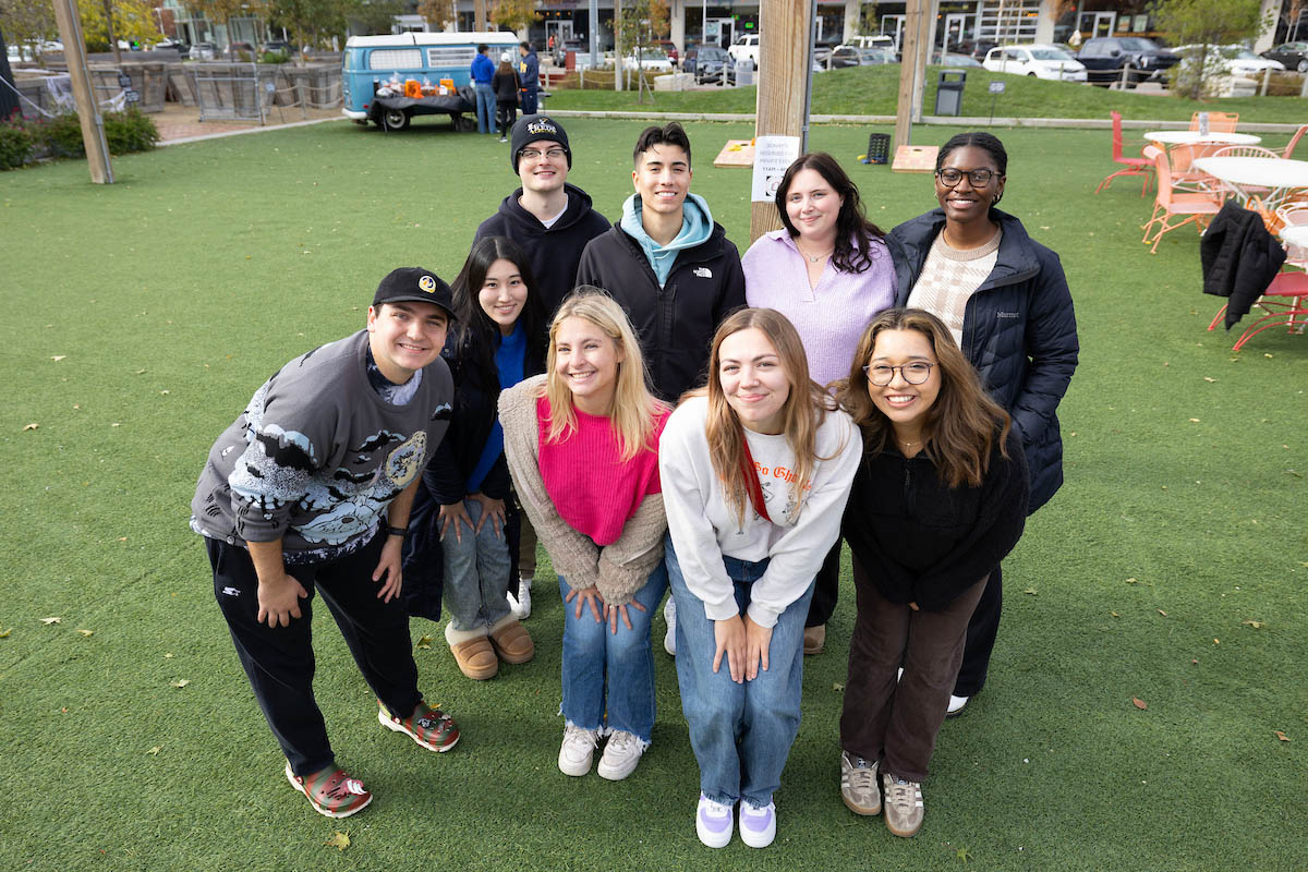 A group of nine student pose together outdoors on a green lawn.
