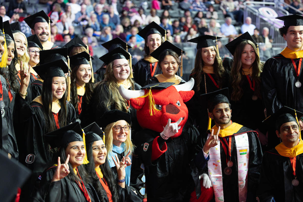A large group of graduates pose for a photo with Durango on the arena floor during commencement.