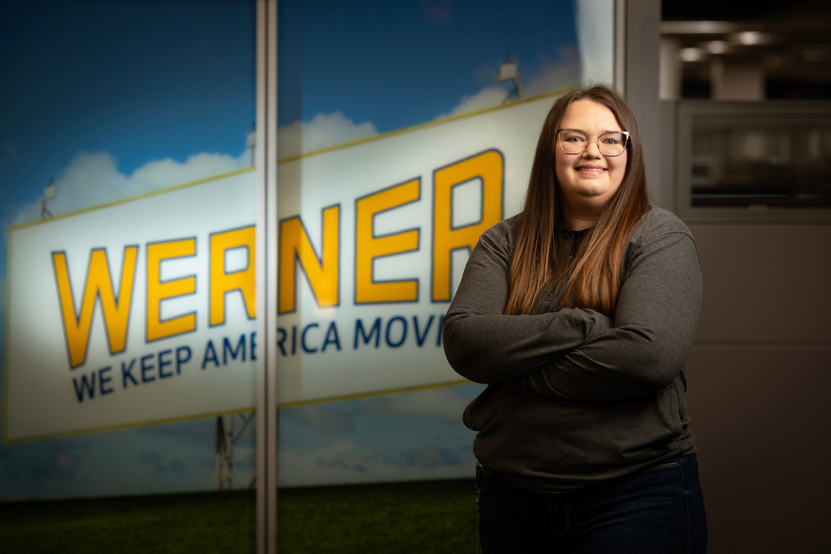 A student stands in front of a lit-up sign reading Werner Enterprises.