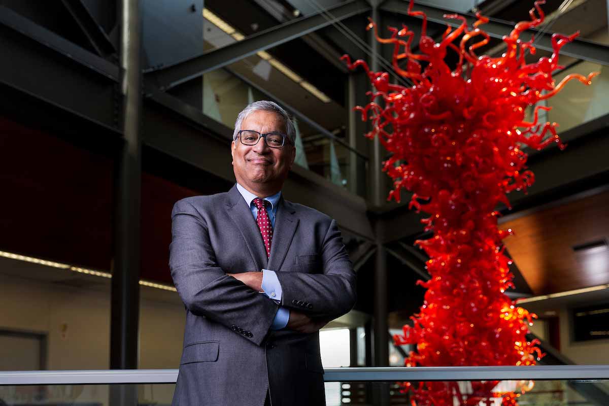 Man in a suit and glasses stands with his arms crossed in a building atrium beside a large red glass sculpture.