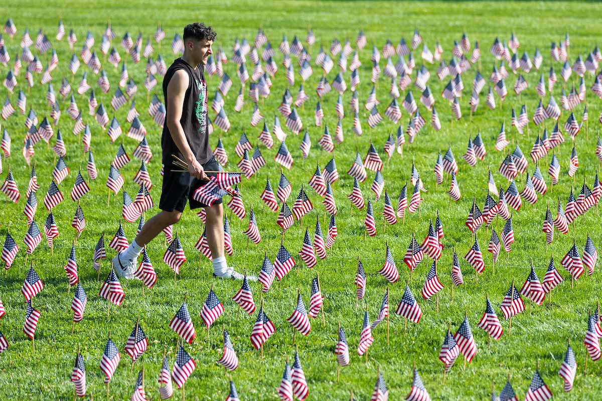 A student walks through a grassy field filled with hundreds of small American flags arranged as a 9/11 memorial. 