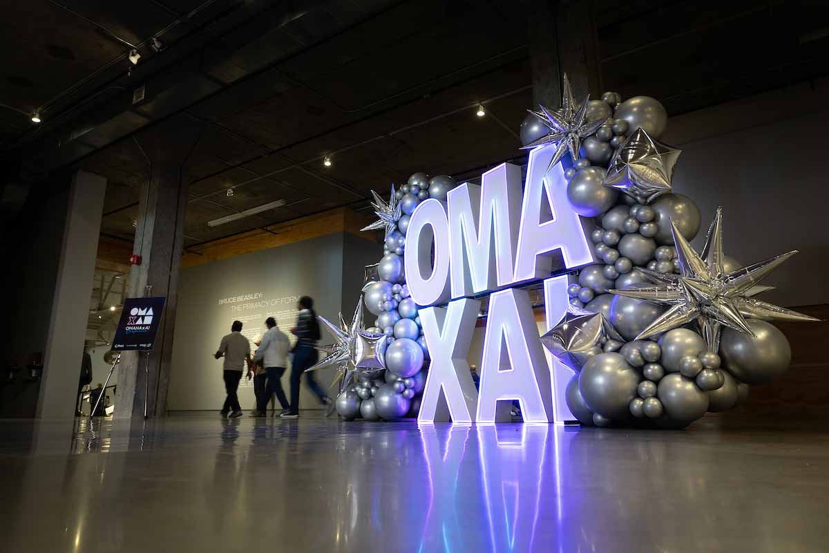 Large illuminated "OMA x AI" display surrounded by silver balloons and metallic star decorations at the entrance to the OMA x AI Conference as attendees walk into the venue. 