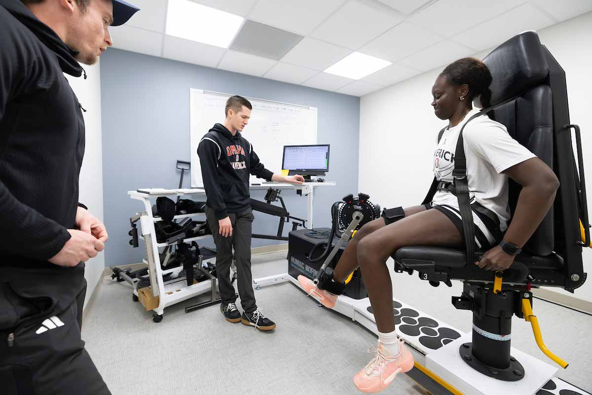 Graduate students perform an athletic assessment on an injured women’s baseketball player, seated and strapped to a chair. 