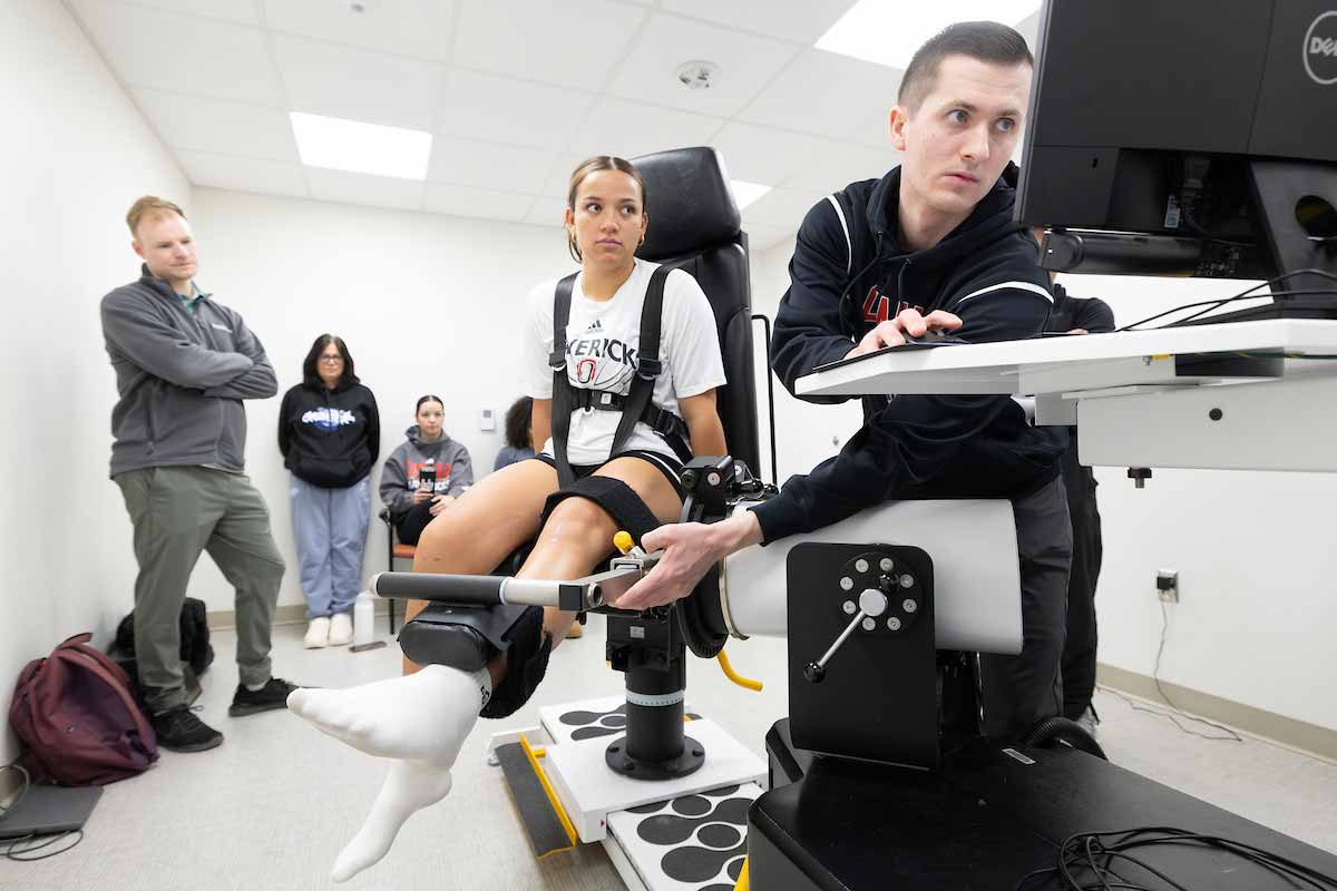 Graduate students perform an athletic assessment on an injured women’s baseketball player, seated and strapped to a chair.  