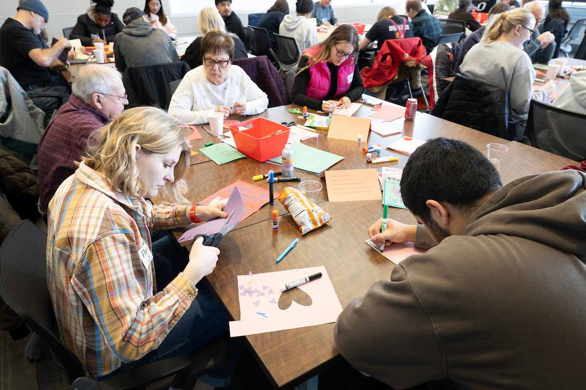 A group of students and elder adults seated at tables covered with crafting materials 