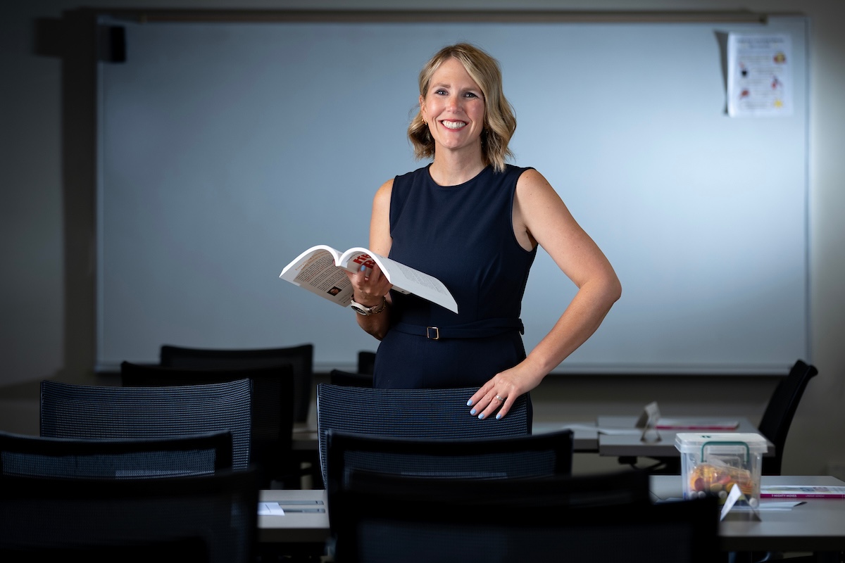 UNO's Jennifer Lemke stands in a classroom holding an open book and smiling toward the camera.