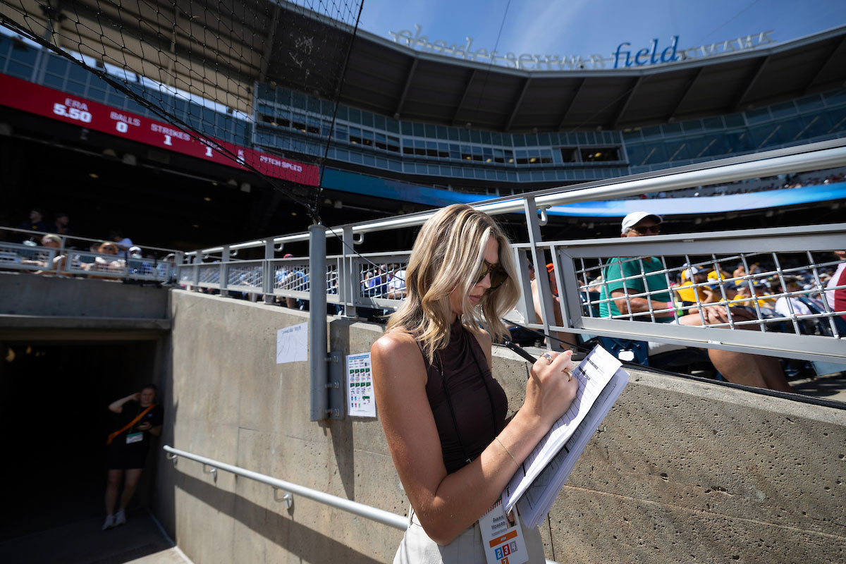 A woman writes in a notebook next to the stands in a baseball stadium.