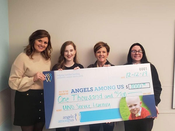 four women stand together holding a large donation check.
