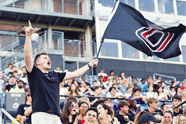 A student waves the UNO flag in a packed stadium student section.