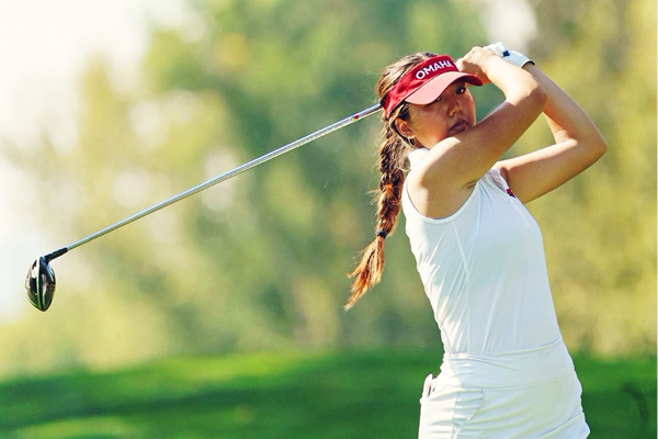 A UNO golfer swings a club on a green golf course.