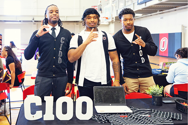Students pose at a Greek life event table indoors.