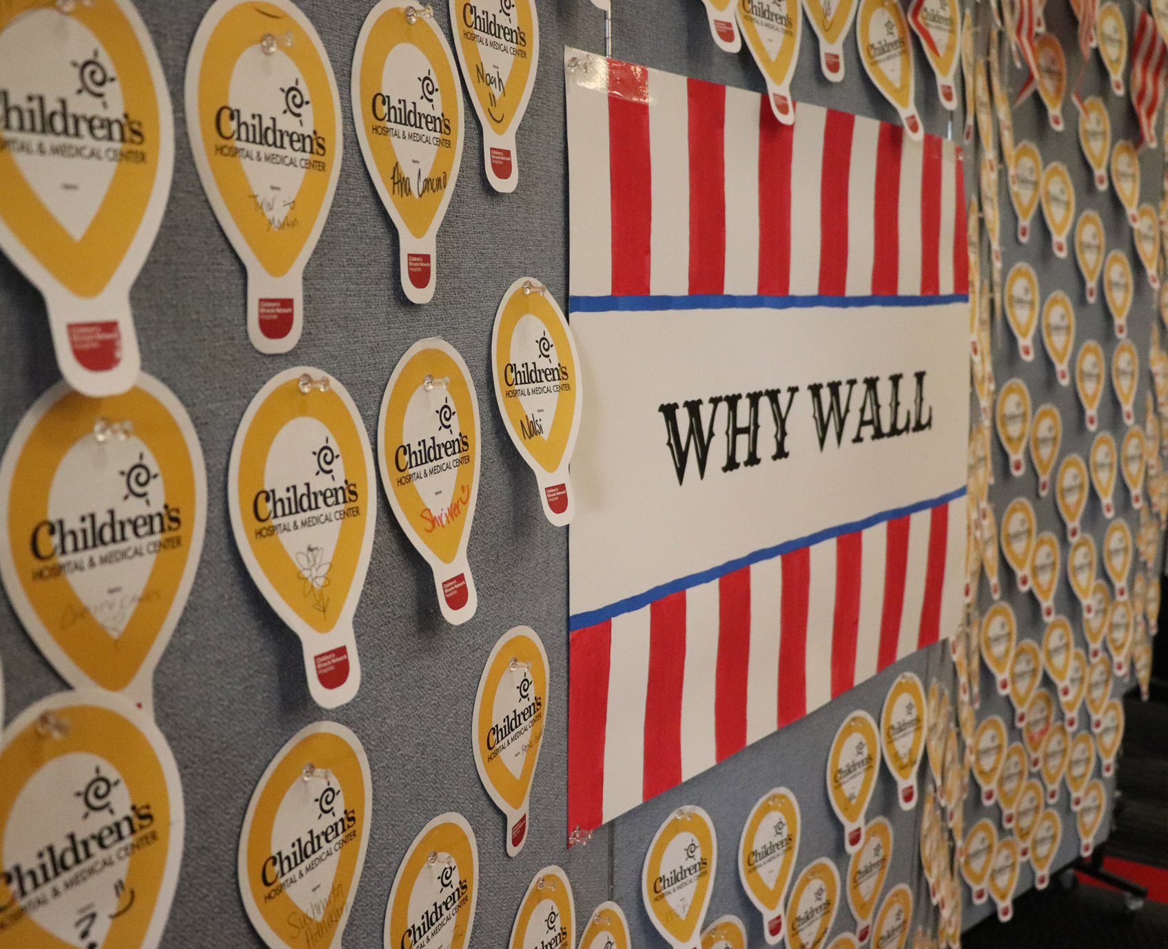 Bulletin board labeled "WHY WALL" with red-and-white stripes, surrounded by many yellow Children’s Hospital & Medical Center paper cutouts pinned in rows.